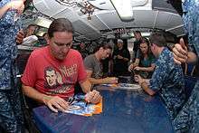 Two men signing autographs in a crowded submarine